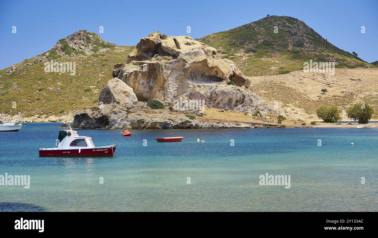 Una baia tranquilla con rocce e barche in acque cristalline sotto un cielo soleggiato, Petras Beach, Kalikatsou Rocks, Patmos, Dodecaneso, isole greche, Grecia, Euro Foto Stock