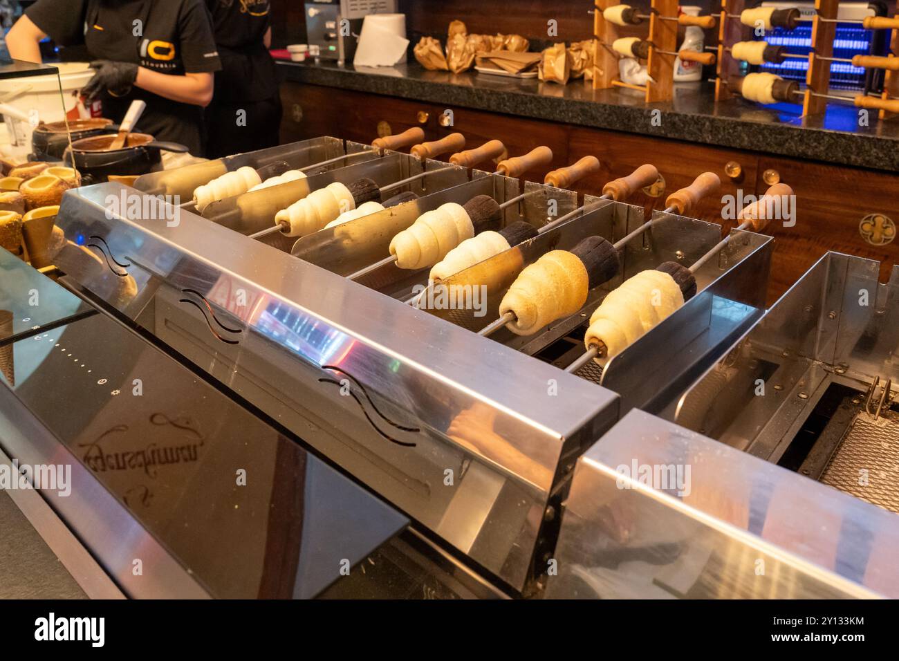 La torta del camino (trdelnik) viene cotta e avvolta intorno a un tubo di ferro caldo sopra un carbone caldo all'interno di un negozio di Praga Foto Stock