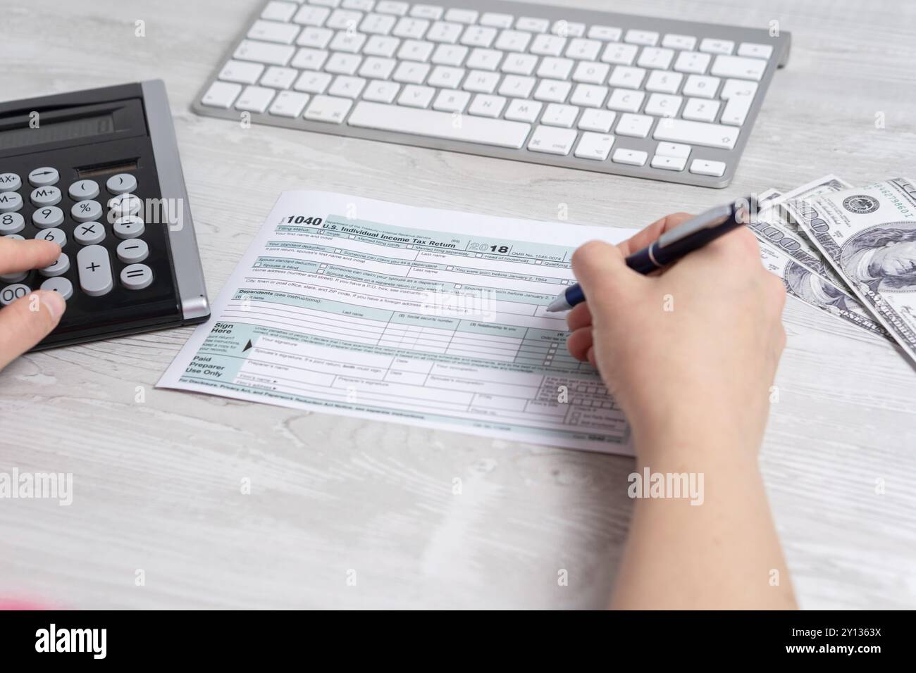 Punto di vista foto di donna e di calcolo e il riempimento di noi sotto forma di imposta accanto alla tastiera del computer e forma fiscale 1040. 15 aprile 2019 giornata fiscale Foto Stock