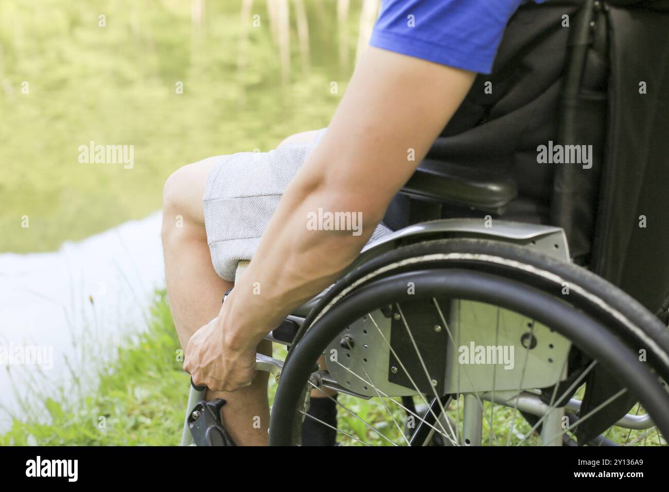 Giovane disabile o handicappato seduto su una sedia a rotelle in natura che gira e tiene le ruote Foto Stock