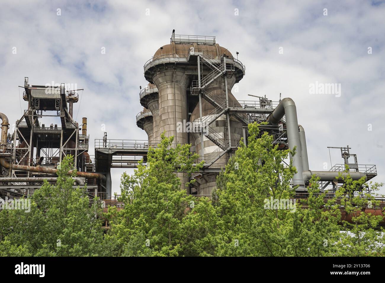 Impianto industriale con grandi tubi e strutture metalliche, circondato da alberi sotto un cielo nuvoloso, Duisburg, Renania settentrionale-Vestfalia, Germania, Europa Foto Stock