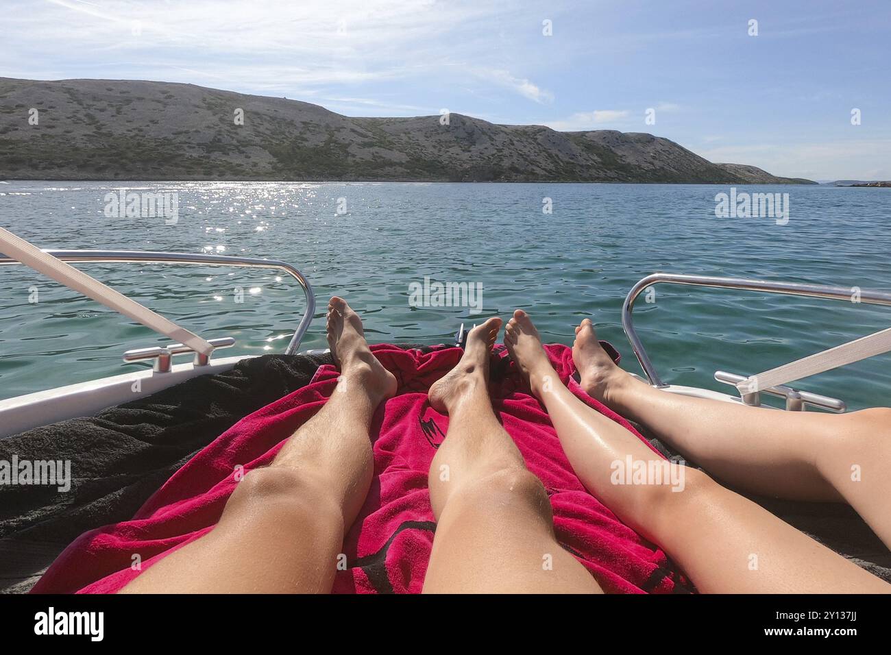 Vista sulle gambe di uomo e donna sdraiate sullo yacht con mare blu tirchese e spiaggia con palme verdi sullo sfondo. Coppia eterosessuale nell'estate di lusso Foto Stock