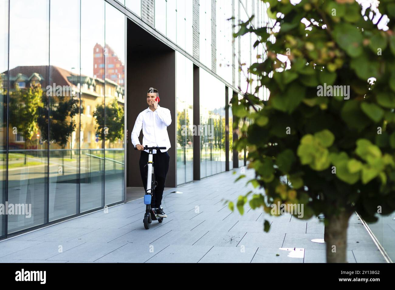 Giovani e casual uomo d affari di equitazione scooter elettrico e parlare sullo smartphone nella città Foto Stock