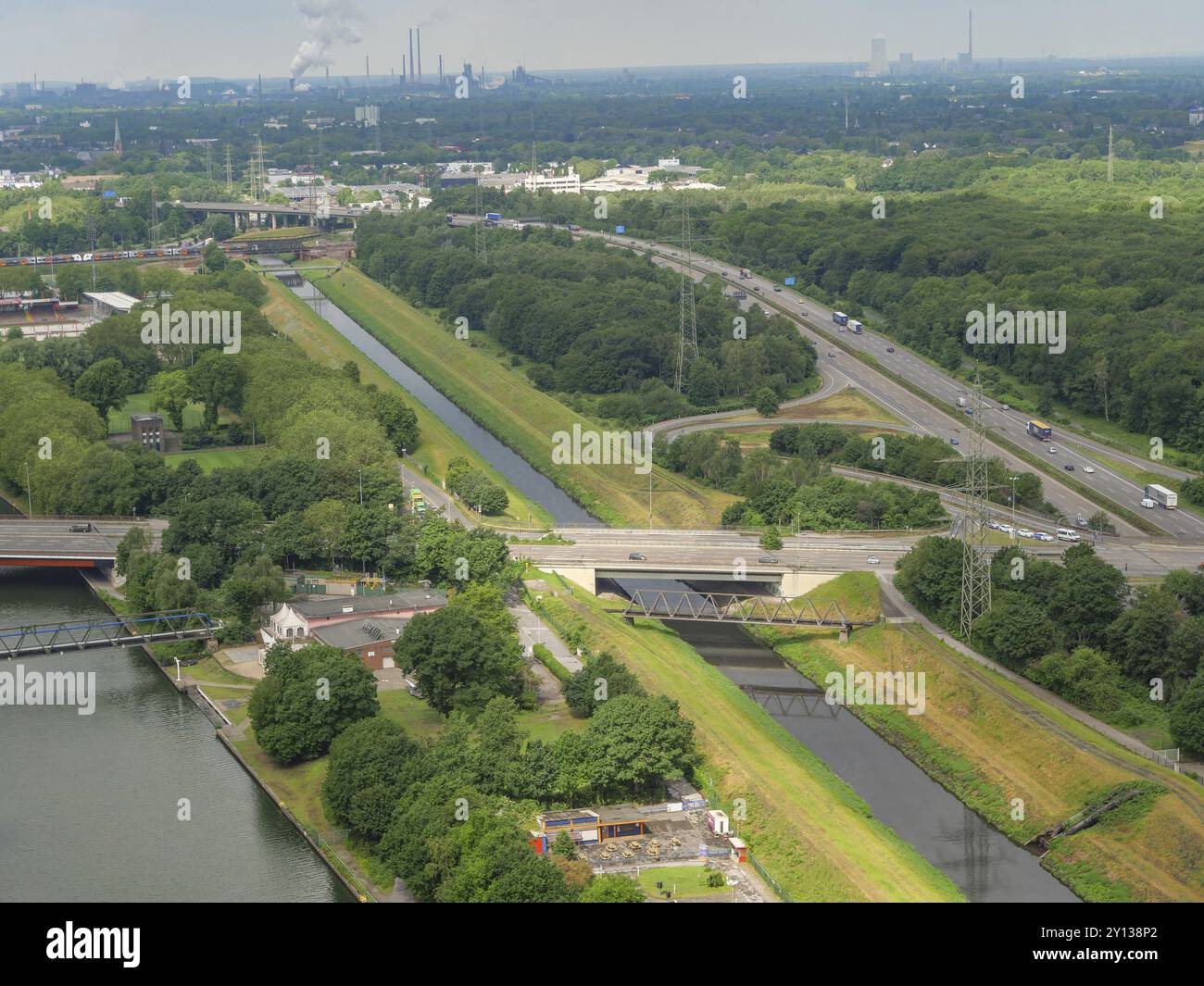Un'autostrada e un canale che corrono in parallelo, incastonati in alberi verdi. Vista dall'alto delle aree industriali sullo sfondo, oberhausen, zona della ruhr, tedesco Foto Stock