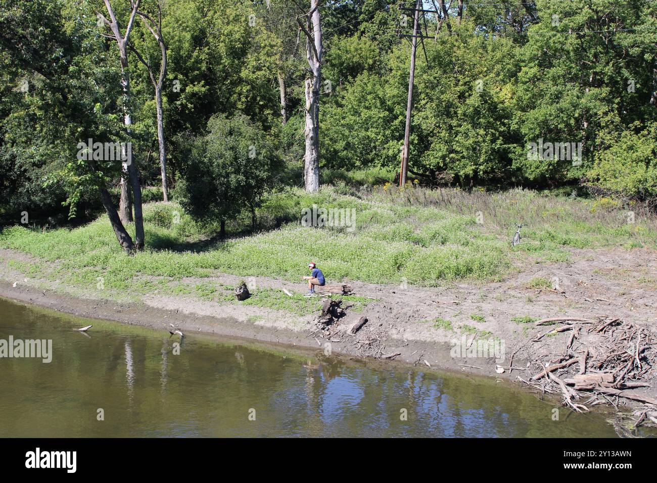 Persona seduta su un tronco con una bicicletta sullo sfondo sulle rive del fiume Des Plaines a Iroquois Woods, Park Ridge, Illinois Foto Stock