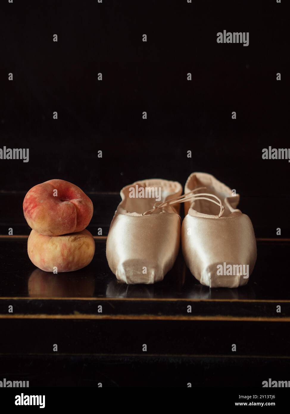 Due pesche di fico accanto alle scarpe White Point su un piano nero: Natura morta verticale Foto Stock