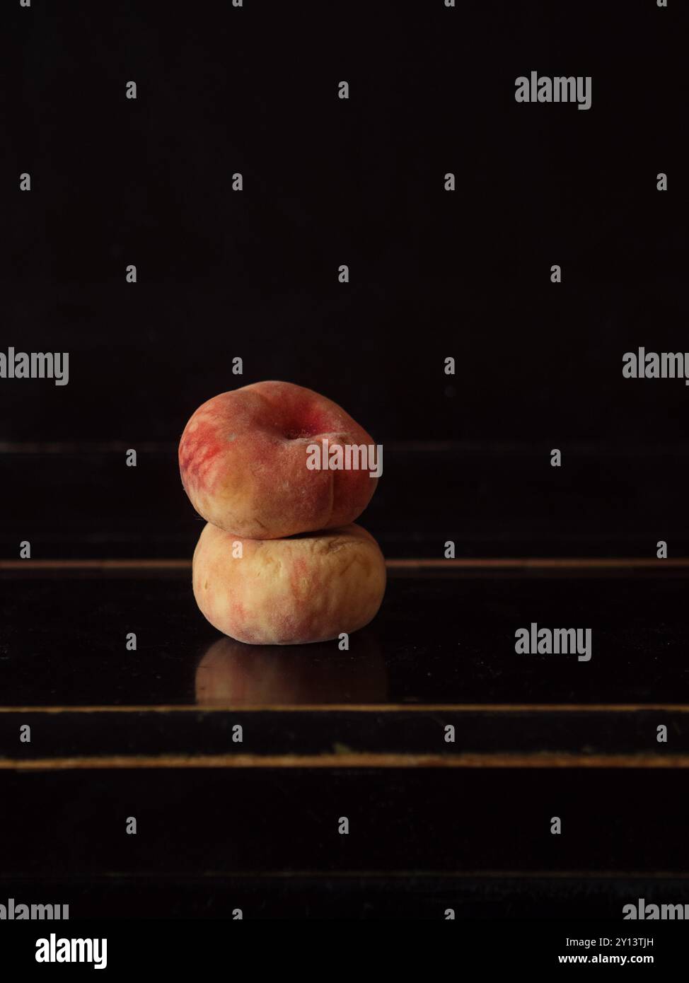 Natura morta minima: Due pesche di fico impilate su un piano nero Foto Stock