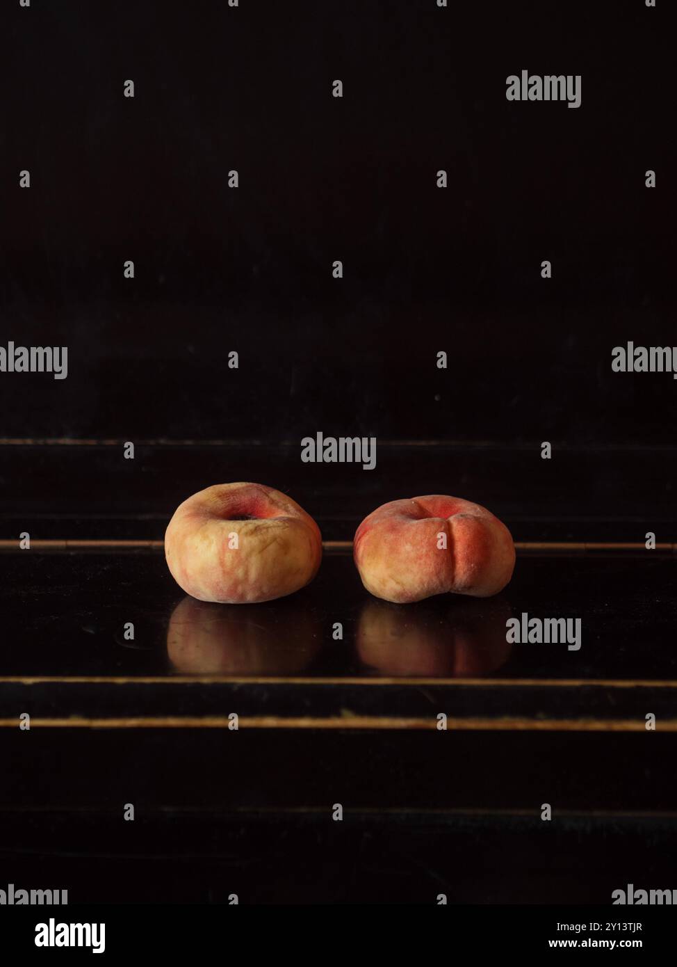 Due pesche di fico affiancate su un piano nero: Natura morta minima verticale Foto Stock
