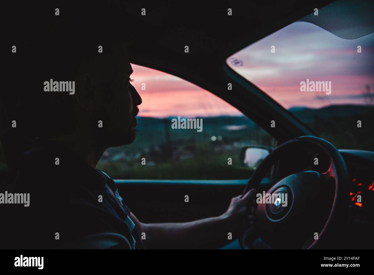 un uomo che guida un'auto in un bellissimo paesaggio al tramonto Foto Stock