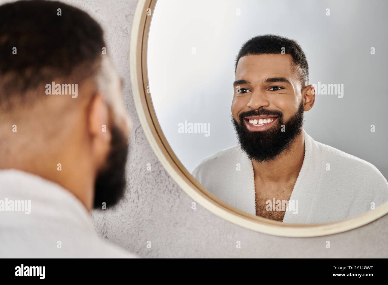 Un uomo sorridente si ammira allo specchio mentre si rilassa a casa. Foto Stock