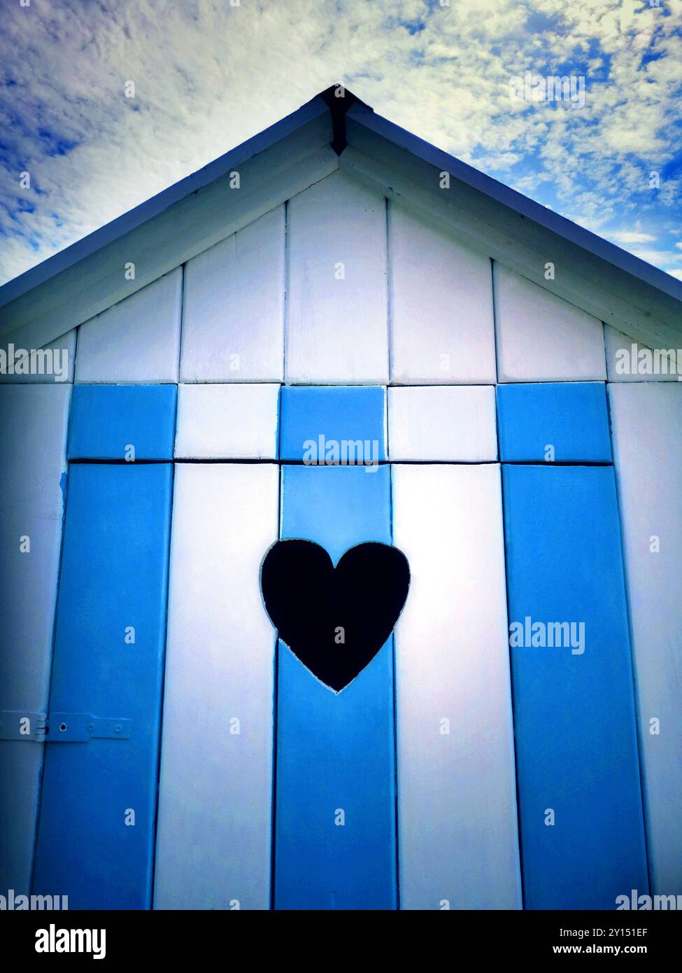 L'incantevole capanna sulla spiaggia presenta una fessura a forma di cuore e vivaci strisce blu e bianche sullo sfondo del cielo limpido Foto Stock