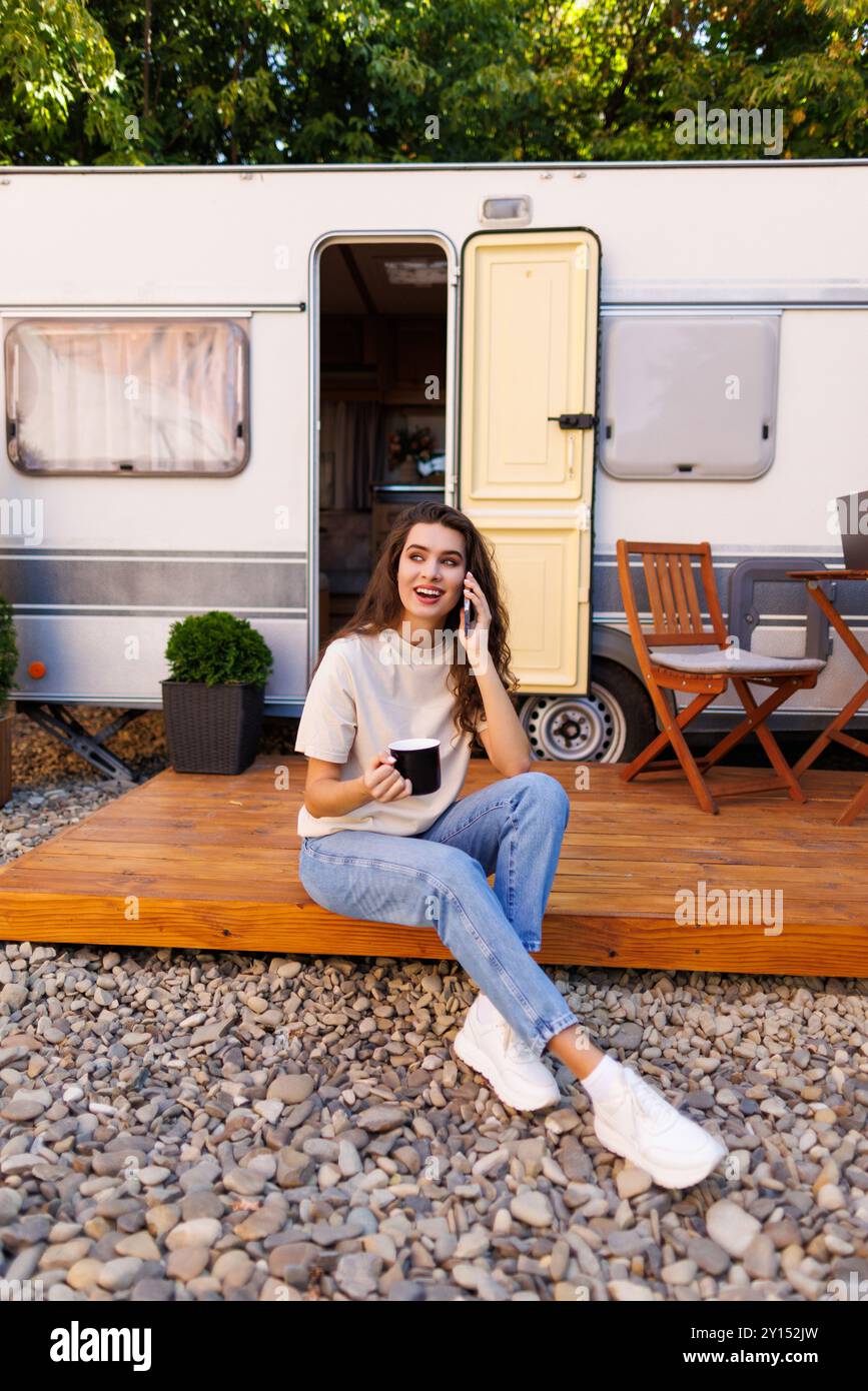 Giovane donna che viaggia da sola in camper a casa in viaggio con uno smartphone Foto Stock