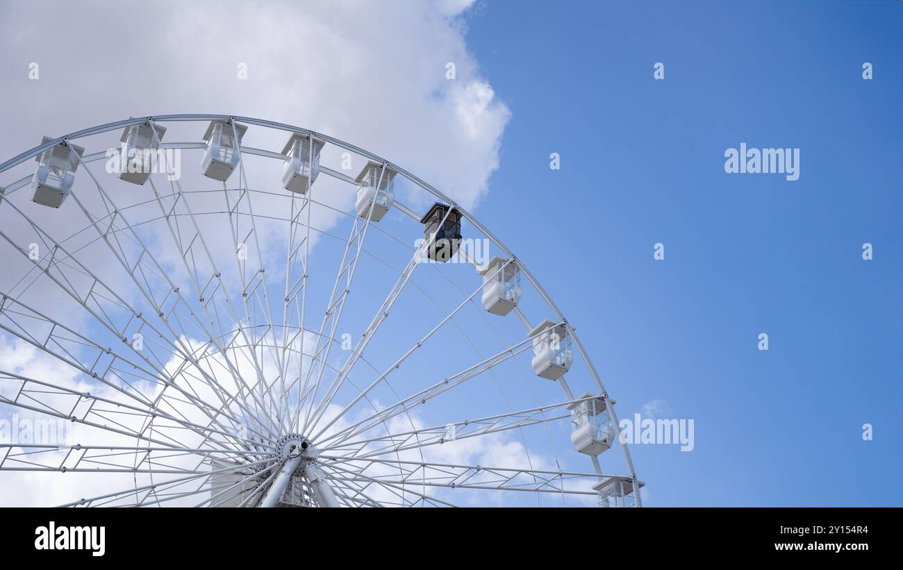 Vista parziale di una ruota panoramica con le cabine bianche e una nera in un parco divertimenti contro un cielo azzurro. Concetto di parco divertimenti Foto Stock
