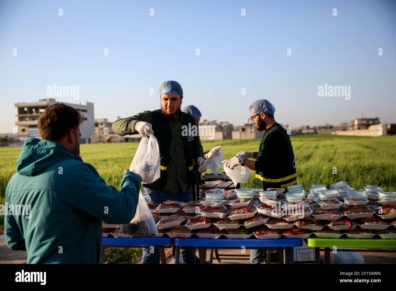 Idlib, Siria. 19 aprile 2022. Varie organizzazioni distribuiscono pasti iftar e succhi di tamarindo e bevande liquirizie ai residenti dei campi di sfollamento vicino a Sarmada, nel governatorato di Idlib, durante il Ramadan. Le difficoltà incontrate dagli sfollati residenti nei campi della roccaforte dell'opposizione di Idlib hanno esacerbato la crisi fiscale in Turchia e la caduta della lira turca, nonché la crisi Ucraina in corso e le conseguenti carenze alimentari Foto Stock