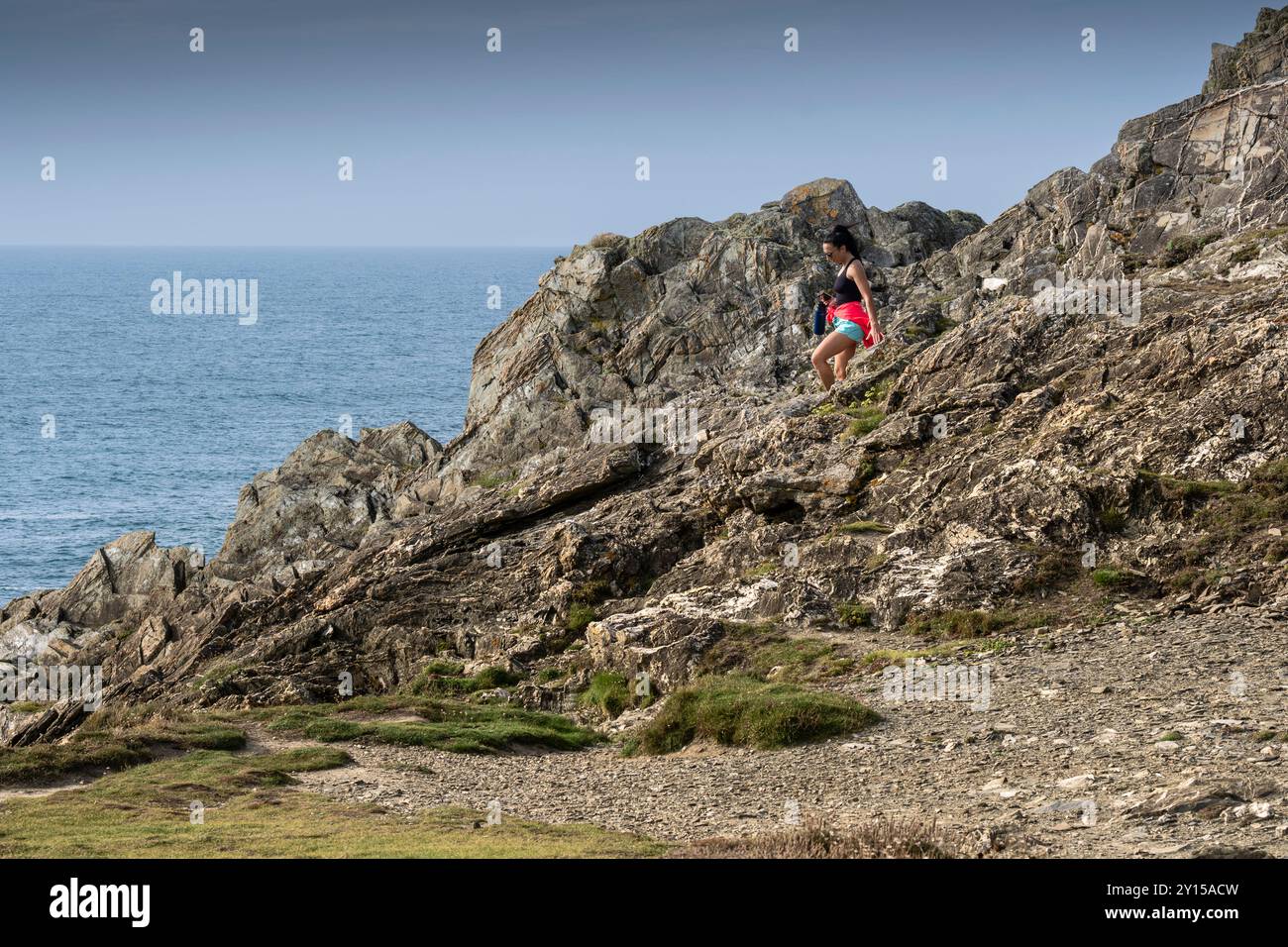 Una vacanziera che cammina con attenzione lungo le scogliere rocciose di Pentire Point East sulla costa di Newquay in Cornovaglia nel Regno Unito, in Europa. Foto Stock