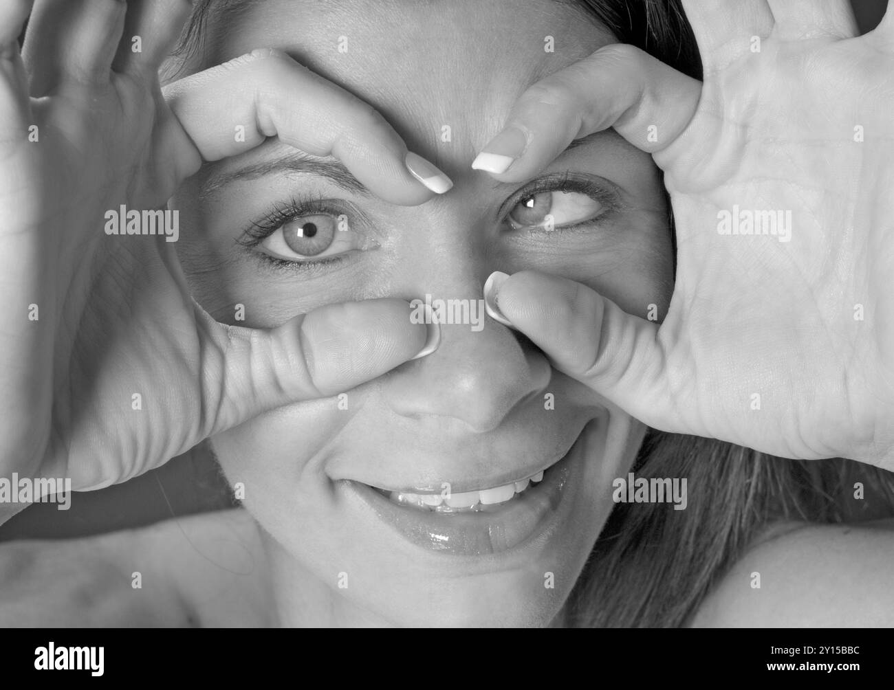 Primo piano di una bella donna caucasica, 30 - 35 anni, che guarda giocosamente attraverso le dita e fa i volti, Stati Uniti. Foto Stock