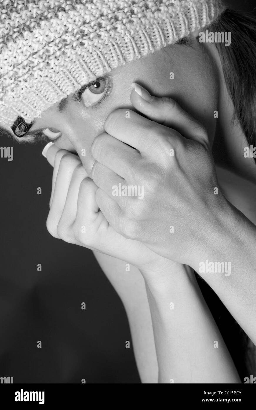 Spaventata donna caucasica (20-25 anni) che indossa un cappello da toboga, coprendo la bocca con pugni chiusi, esprimendo sintomi di ansia. STATI UNITI. Foto Stock
