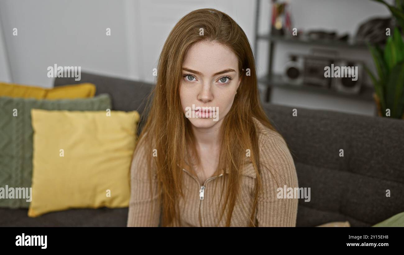 Una giovane, bella donna caucasica con i capelli biondi siede con cura in un salotto moderno, il suo sguardo calmo e penetrante. Foto Stock