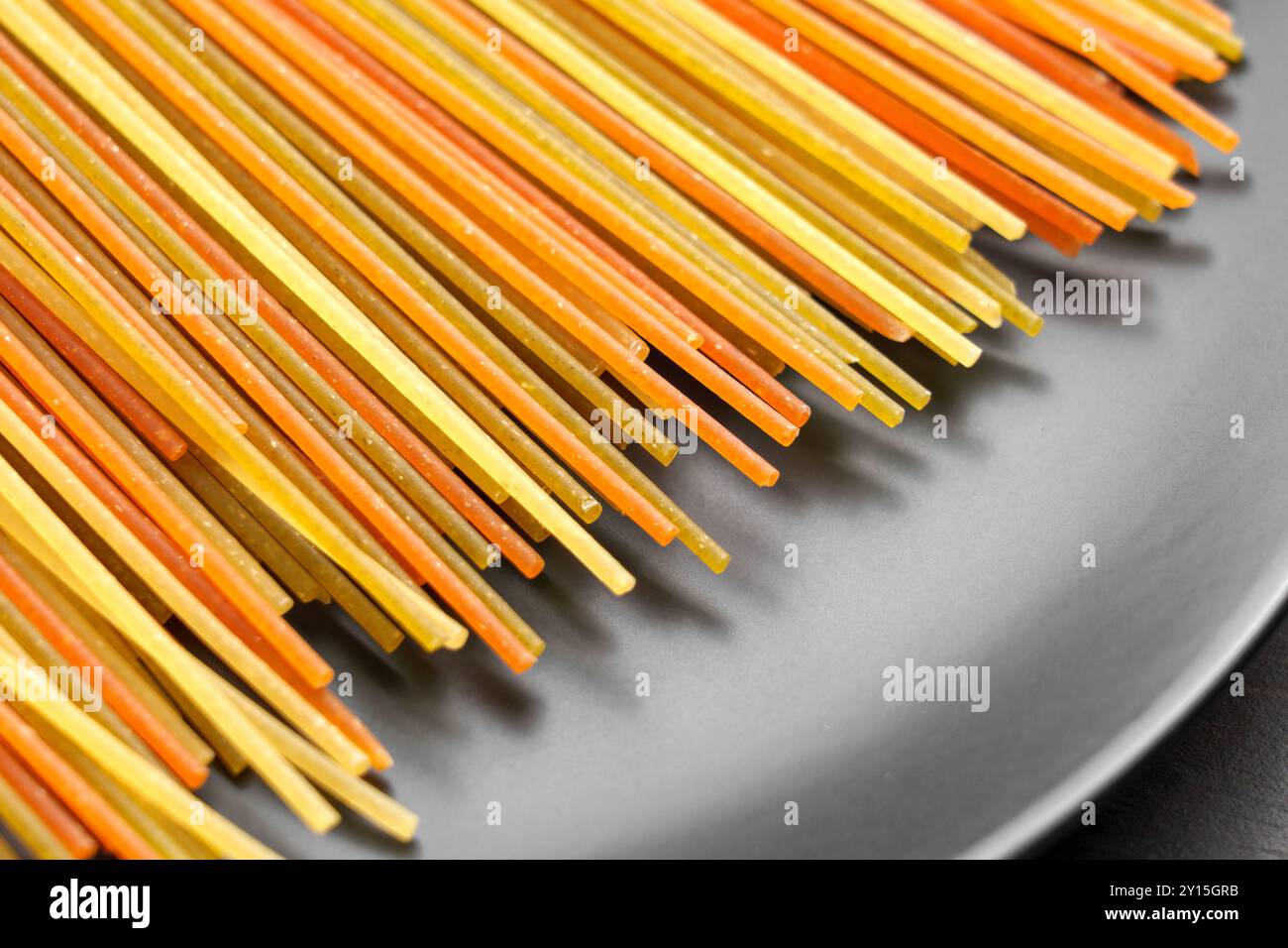 Spaghetti di pasta cruda, caratterizzati da colori sorprendenti derivati da ingredienti naturali, elegantemente disposti su un moderno piatto grigio Foto Stock