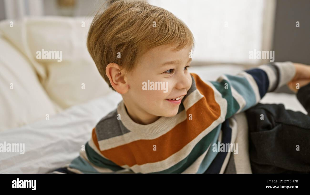 Sorridente biondo che si rilassa casualmente su un letto bianco in una stanza soleggiata, irradiando innocenza e gioia. Foto Stock