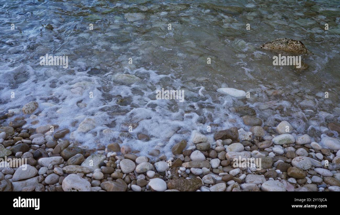 Litorale di ciottoli con onde dolci che scivolano sulle rocce in una giornata tranquilla e limpida che mostra una splendida scena costiera Foto Stock
