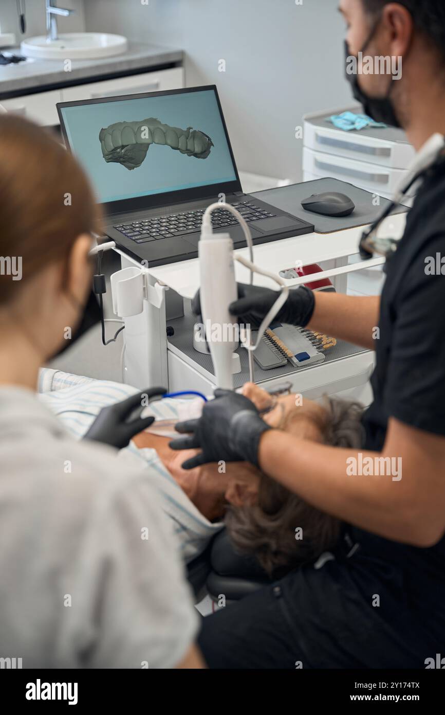 Dentista maschio con assistente che cura i denti di anziana signora Foto Stock