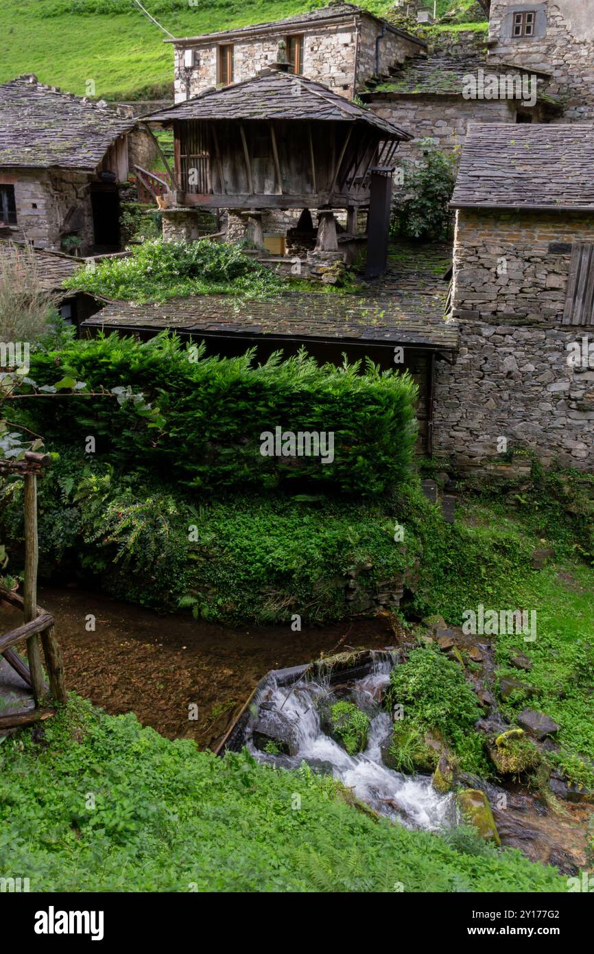 Cottage rustici di campagna con edificio in pietra, ruscello, passerella e vegetazione lussureggiante. Ensemble Etnografico di Teijóis, Asturie, Spagna Foto Stock