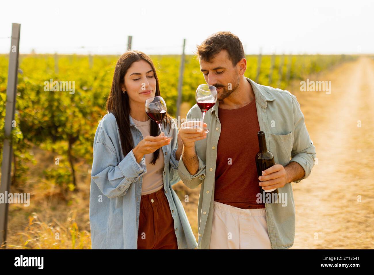 Sotto il caldo bagliore del sole che tramonta, una coppia condivide le risate sorseggiando del vino in un pittoresco vigneto, creando ricordi preziosi tra le file Foto Stock