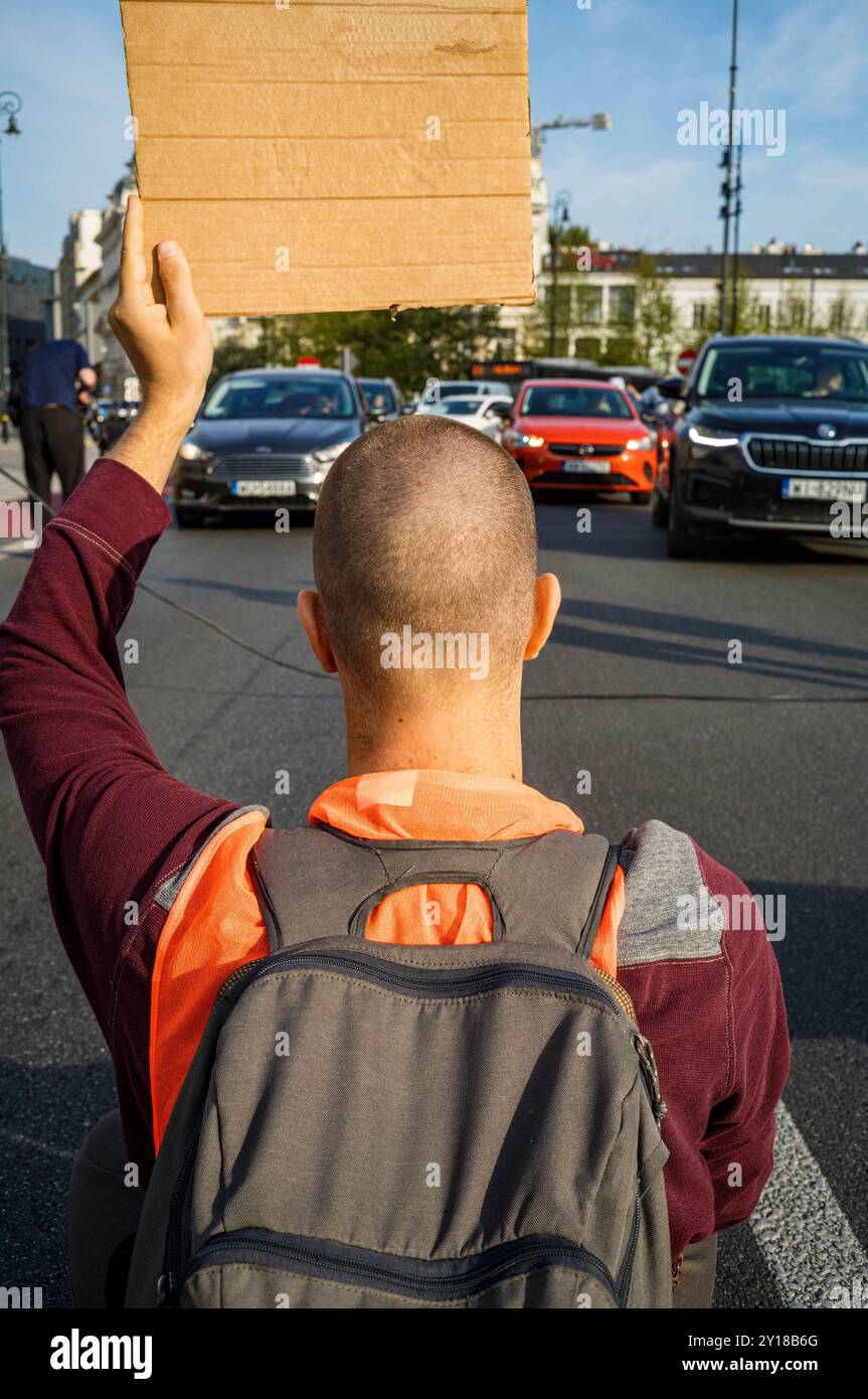 Un manifestante tiene un cartello mentre blocca la strada. La mattina del 5 settembre, un gruppo di attivisti di Ostatnie Pokolenie (l'ultima generazione) blocca la strada sotto la chiesa di Sant'Alessandro sulla piazza delle tre croci di Varsavia. L'azione è una delle tante volte a promuovere opzioni di trasporto pubblico più economiche e più ampie. Il gruppo chiede che il governo sposti il 100% del denaro stanziato per le nuove autostrade verso il trasporto pubblico regionale e introduca un biglietto a basso costo da 50 PLN per il trasporto pubblico in tutta la Polonia. La serie di blocchi stradali si svolge nella settimana in cui Polis Foto Stock