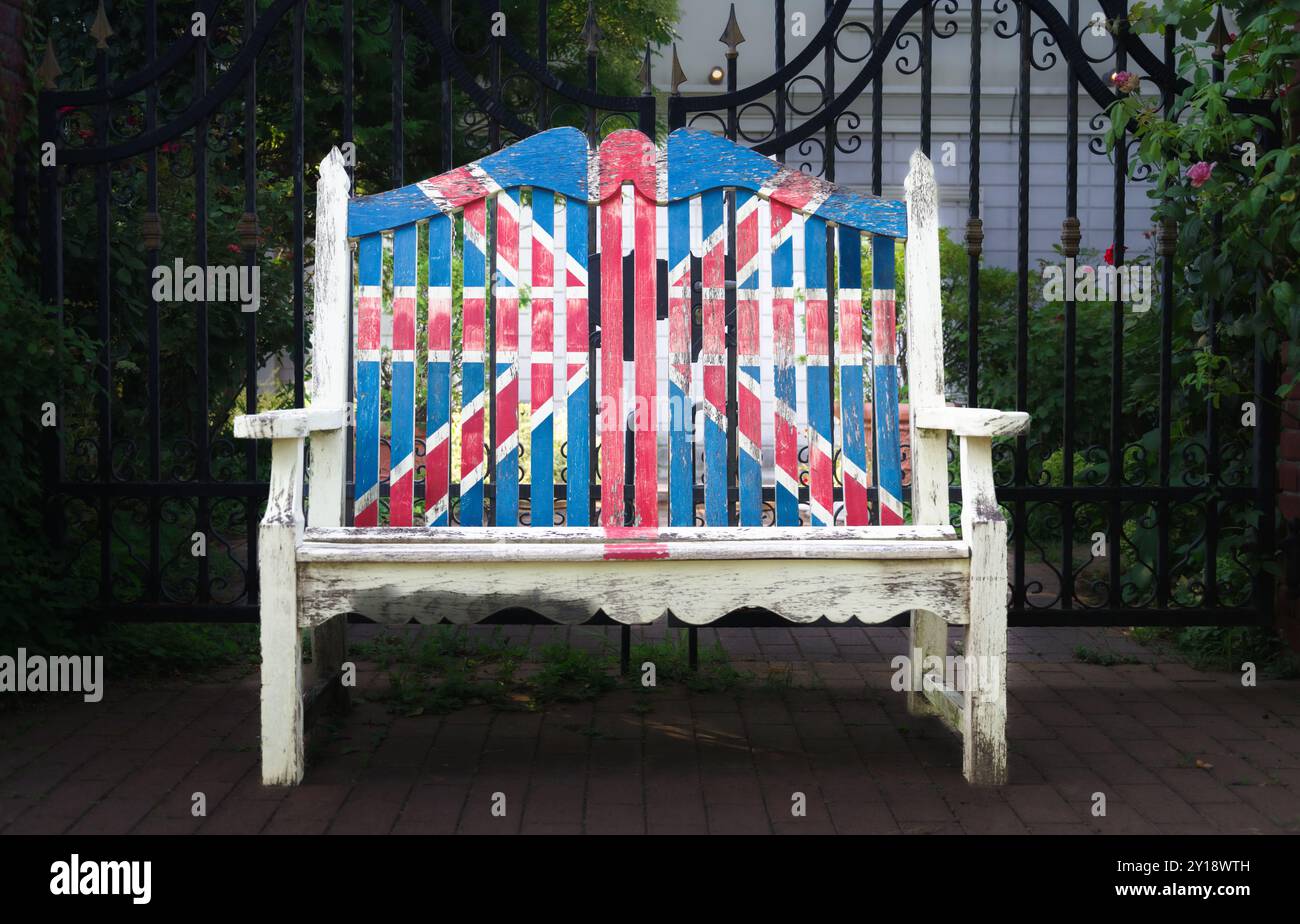 Una panchina bianca intemprata adornata con una sbiadita Union Jack siede graziosamente tra le vibranti fioriture e il verde del Giardino inglese di Yokohama, evocando un'atmosfera di Foto Stock