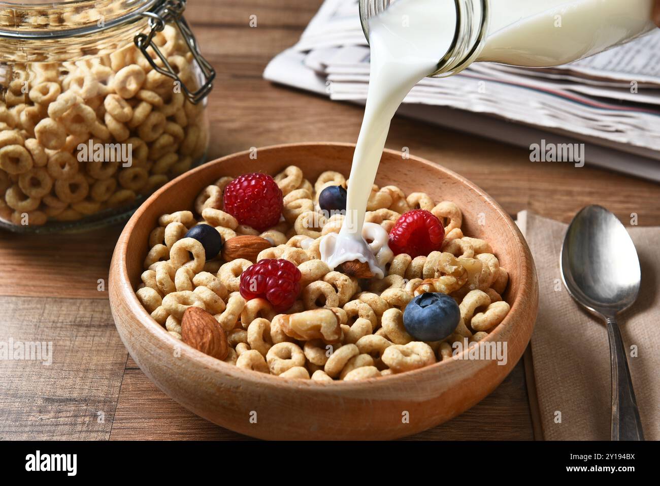 Vista dall'alto su una ciotola di cereali da colazione con mirtilli, lamponi e noci. Una bottiglia di latte viene versata nel recipiente Foto Stock