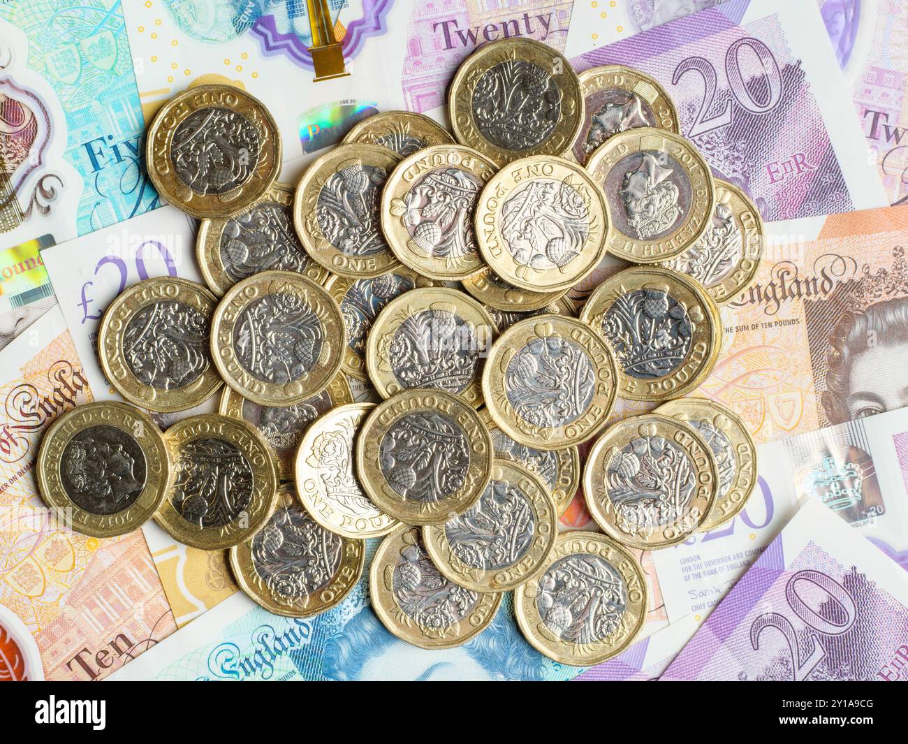 Primo piano di molte monete inglesi pound che poggia su banconote di sterlina denaro contante, Regno Unito Foto Stock