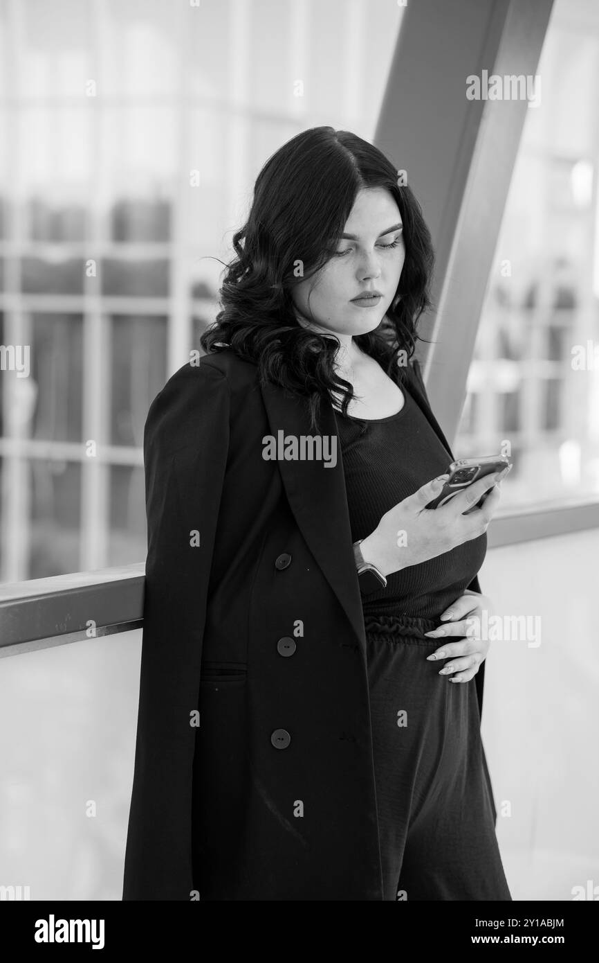 Moderna donna d'affari in una contemplazione attenta con smartphone in bianco e nero. Foto Stock