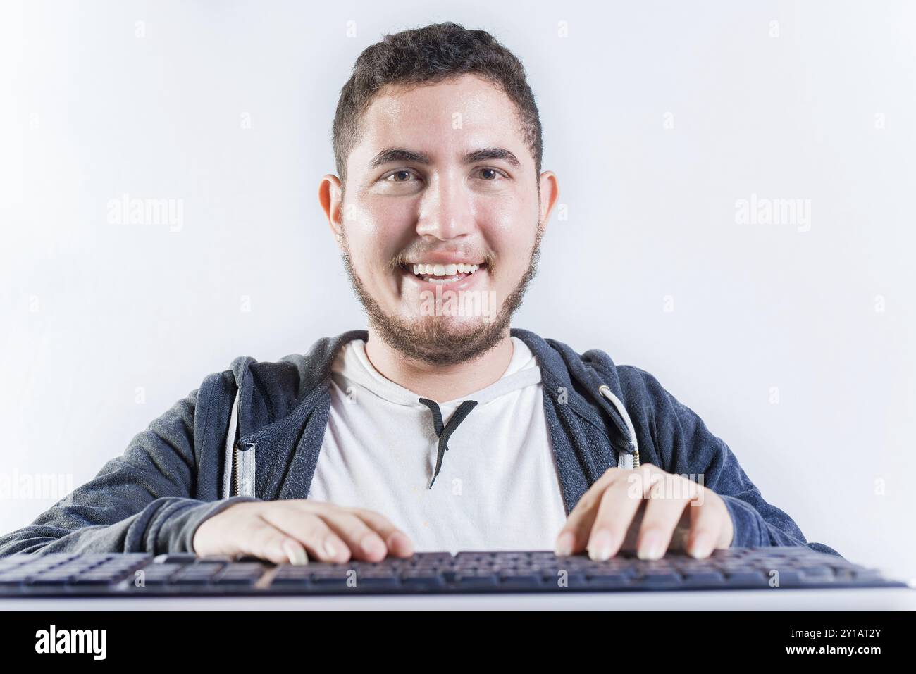 Ritratto dell'uomo nerd davanti alla tastiera. Ragazzo sorridente con le mani sulla tastiera che sorride alla fotocamera Foto Stock