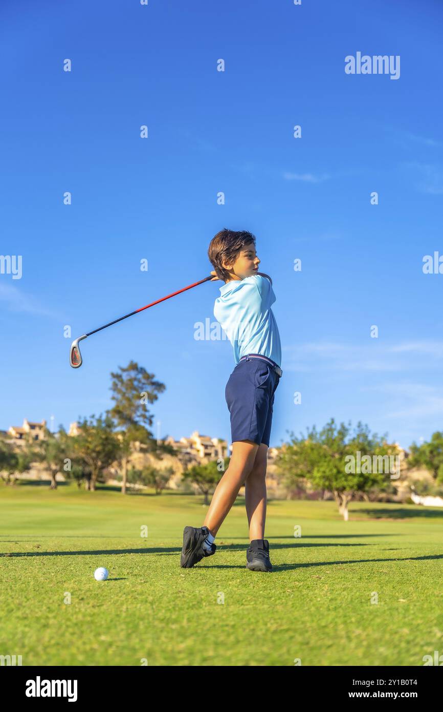 Ritratto verticale laterale di un ragazzo caucasico che esegue un swing perfetto in un campo da golf Foto Stock