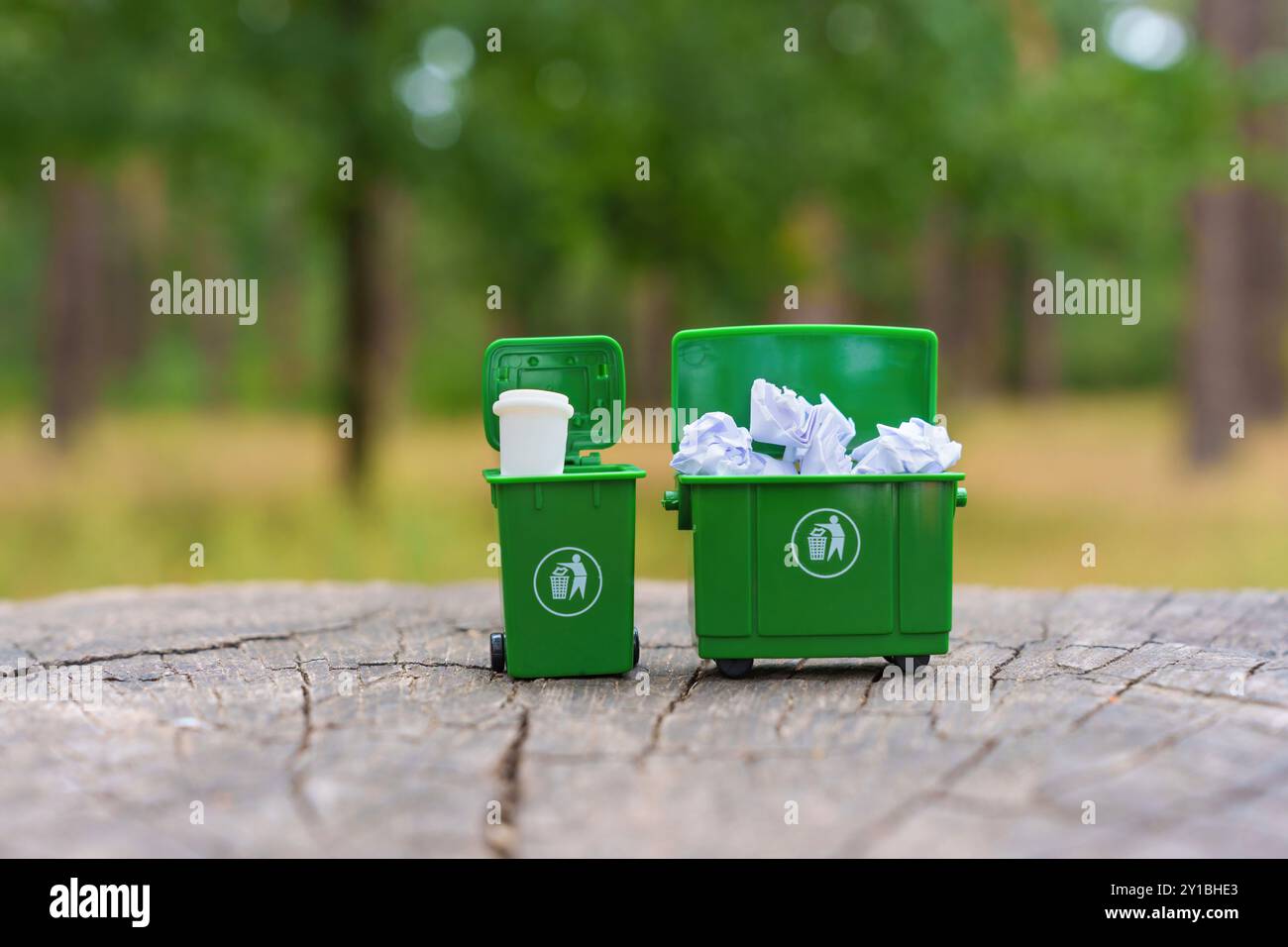 Contenitori di riciclaggio verdi miniaturizzati che presentano un mix di rifiuti di carta e plastica, evidenziando la corretta separazione dei rifiuti. Foto Stock