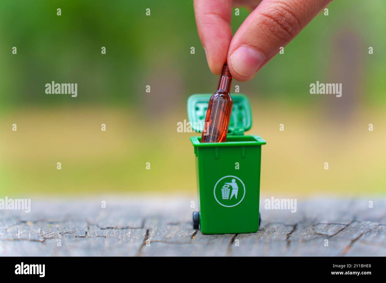 La mano lascia cadere una bottiglia di vetro in un contenitore di riciclaggio verde all'aperto, simboleggiando le abitudini di riciclaggio sostenibile. Foto Stock