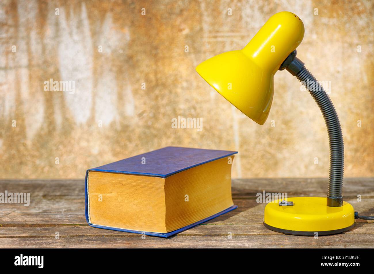 Una lampada da tavolo e un libro su un vecchio tavolo di legno su uno sfondo squallido Foto Stock