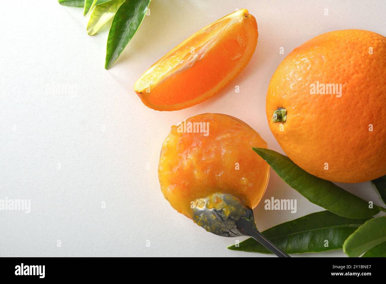 Particolare di marmellata d'arancia in un vaso isolato su un tavolo bianco con frutta intorno e foglie. Vista dall'alto. Foto Stock