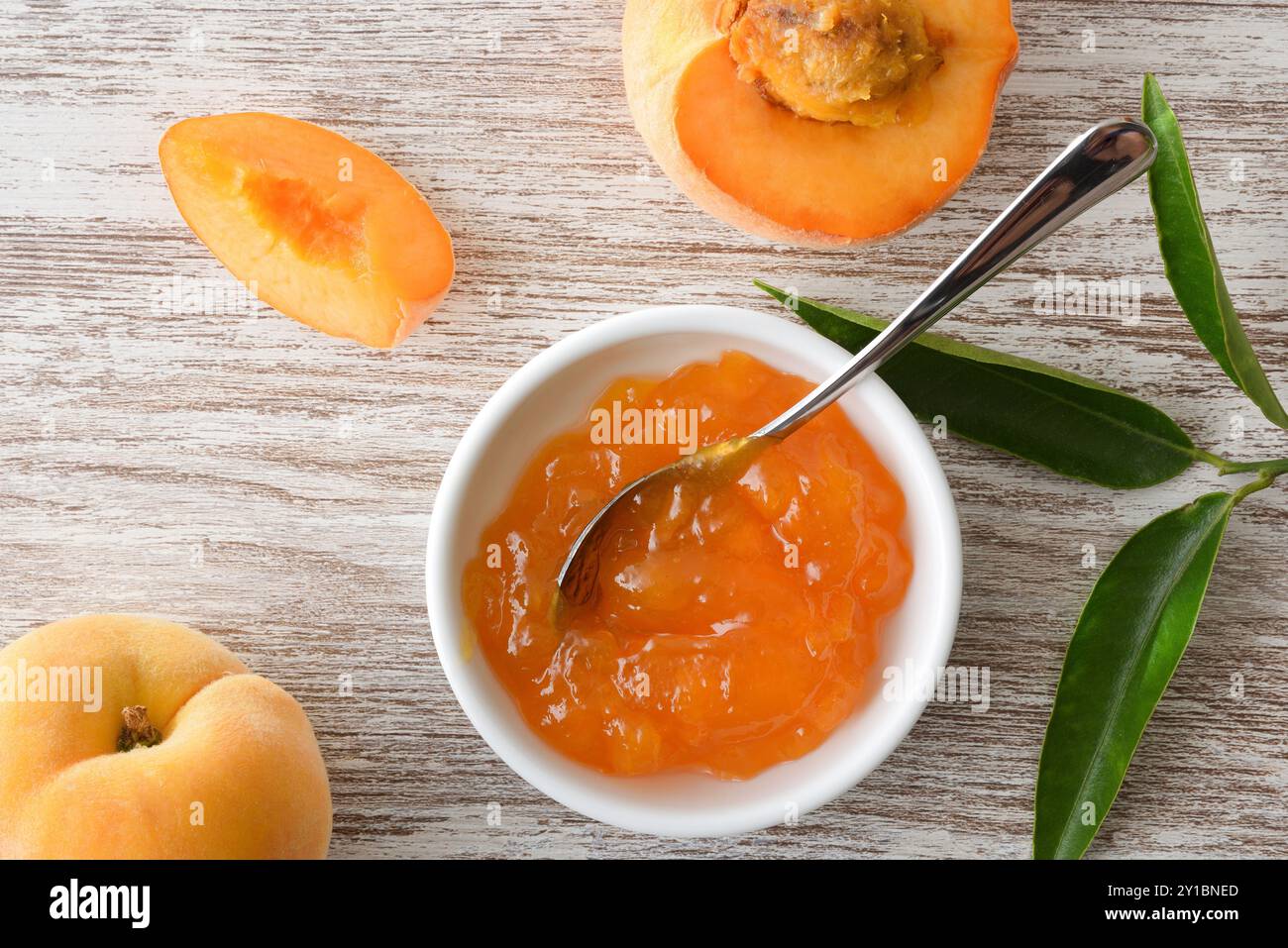Dettaglio della marmellata di pesca in un recipiente e pezzi di frutta su un tavolo di legno. Vista dall'alto. Foto Stock
