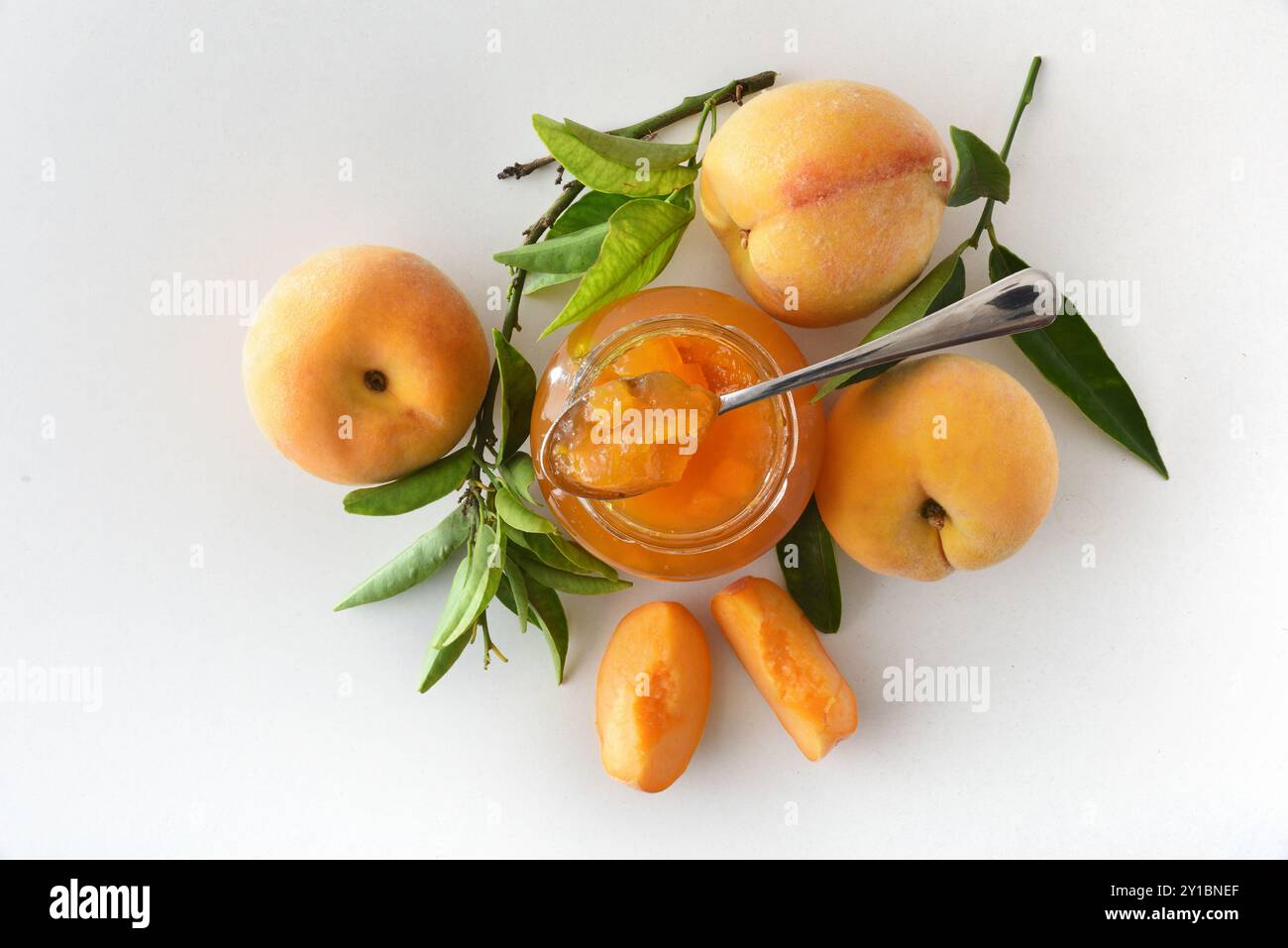 barattolo e pesca pieni di marmellata di prugne e frutta attorno a un tavolo bianco isolato. Vista dall'alto. Foto Stock