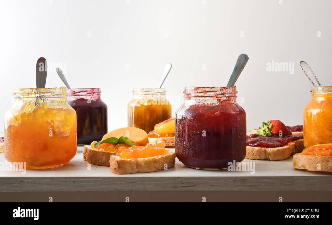 Vasetti pieni di marmellata di vari gusti e fette di pane con marmellata decorata e sfondo bianco isolato. Vista frontale. Foto Stock