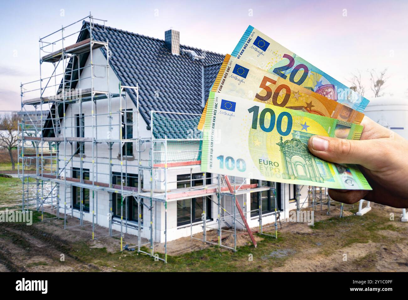 Tenere a mano le banconote in euro davanti a una casa unifamiliare in costruzione Foto Stock