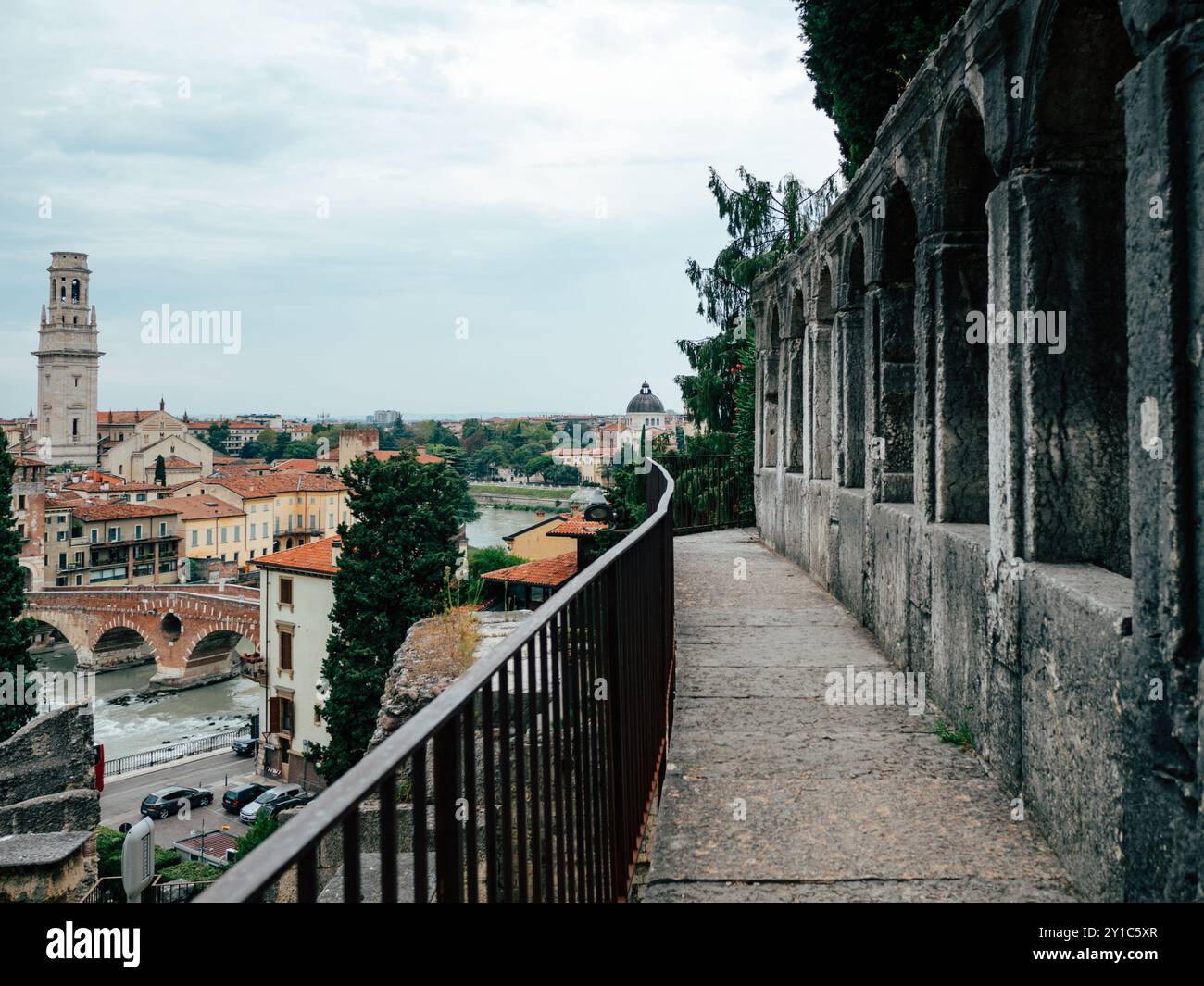 Passeggiando lungo un sentiero acciottolato che si affaccia sul fiume, questa vista mostra la splendida architettura di Verona e i vivaci tetti durante la tarda a Foto Stock