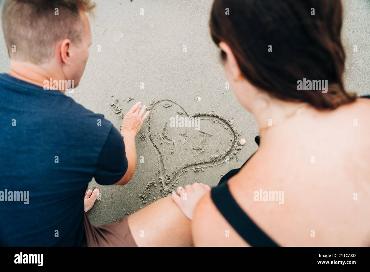Coppia che disegna insieme un cuore nella sabbia, con le iniziali all'interno Foto Stock