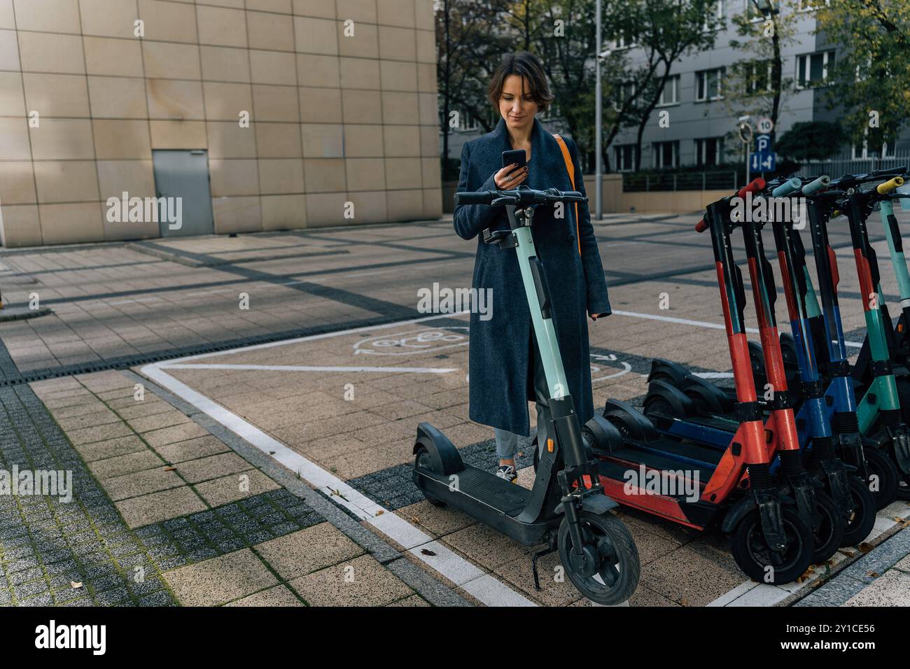 Giovane donna che scansiona il codice QR per noleggiare uno scooter elettrico in un ambiente urbano Foto Stock