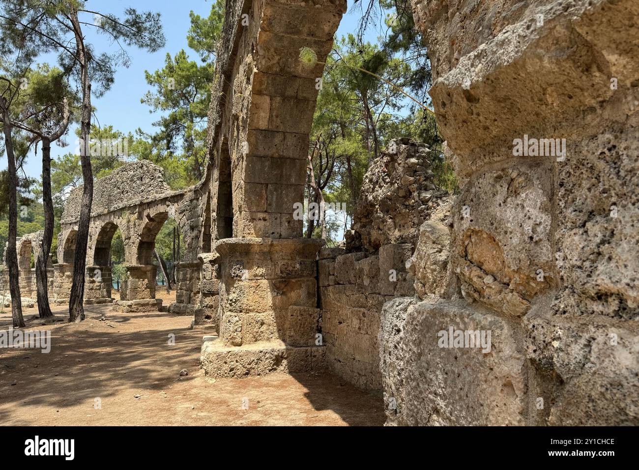 Dettaglio rovine archeologiche dell'antico acquedotto romano a Türkiye, Afrodisia, ponte d'acqua in pietra a due piani tra alberi verdi, natura e villaggi Foto Stock