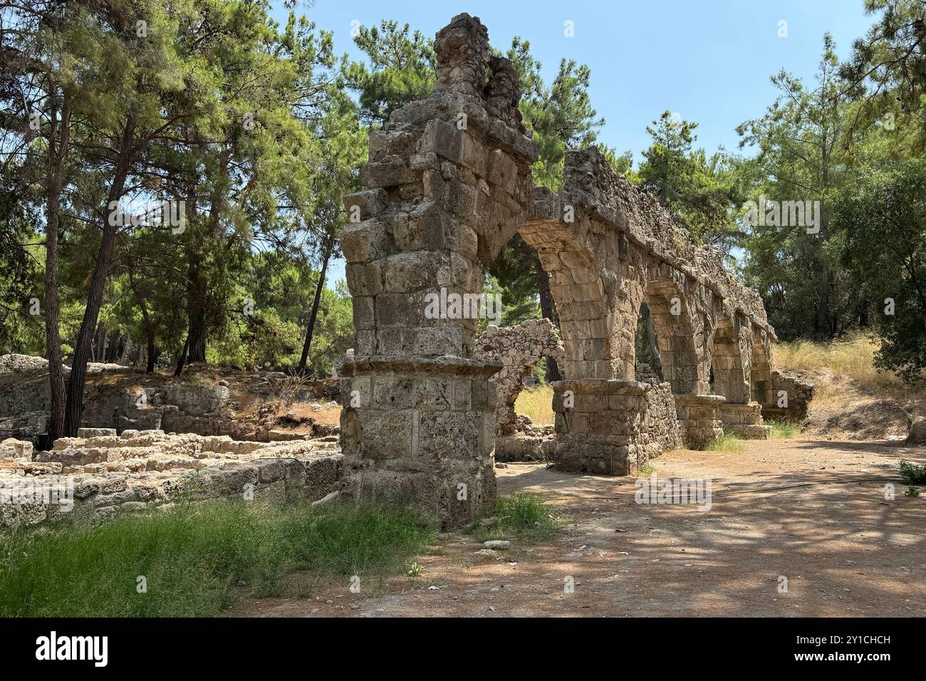 Dettaglio rovine archeologiche dell'antico acquedotto romano a Türkiye, Afrodisia, ponte d'acqua in pietra a due piani tra alberi verdi, natura e villaggi Foto Stock