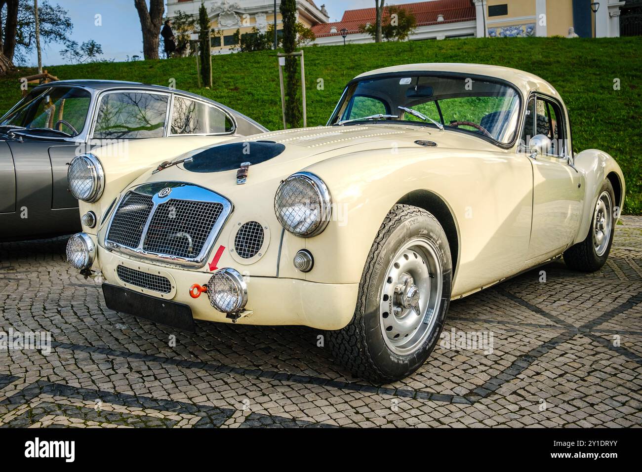 Lisbona, Portogallo - 20 gennaio 2024: Una classica auto sportiva MGA Twin Cam con prese d'aria aggiuntive, gancio di traino e spot luminosi parcheggiati su un sentiero acciottolato vicino al parco verde. Foto Stock