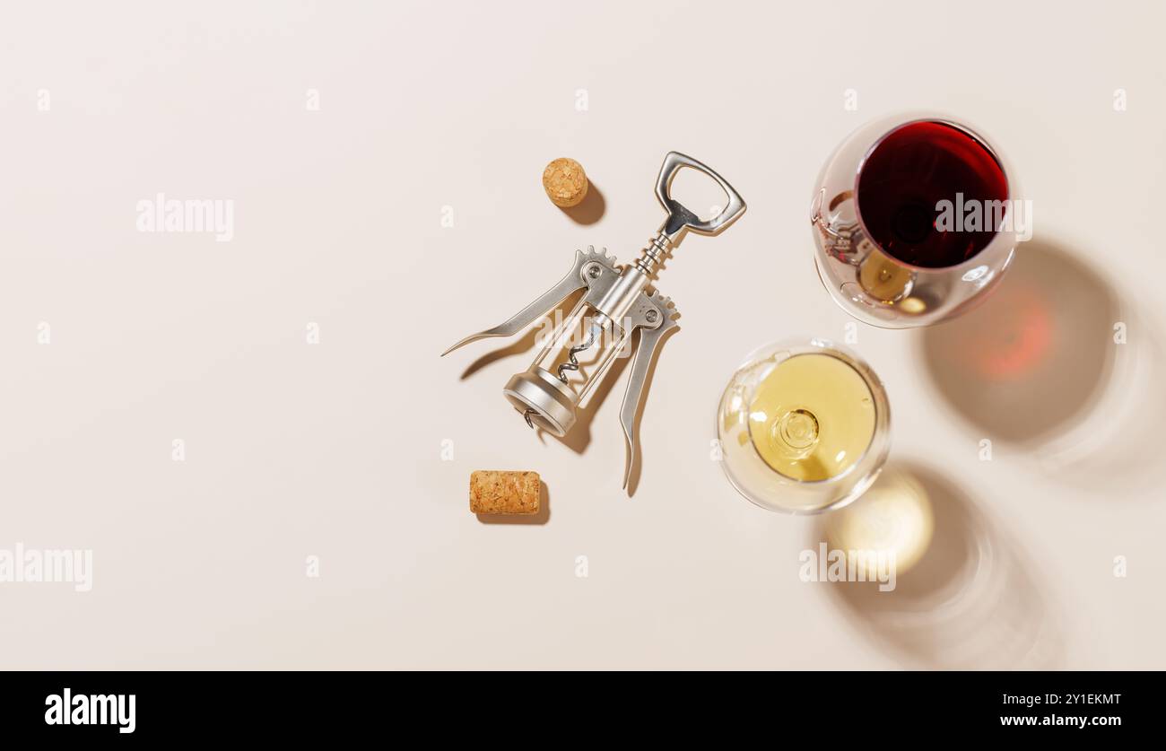Due bicchieri da vino accanto a un cavatappi e diversi tappi di sughero, tutti disposti su uno sfondo luminoso. La luce dura crea ombre nitide, aggiungendo un effetto drammatico Foto Stock